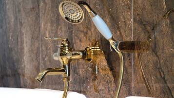 Un baño con ducha y grifo de latón, un lavabo blanco y una pared de madera.