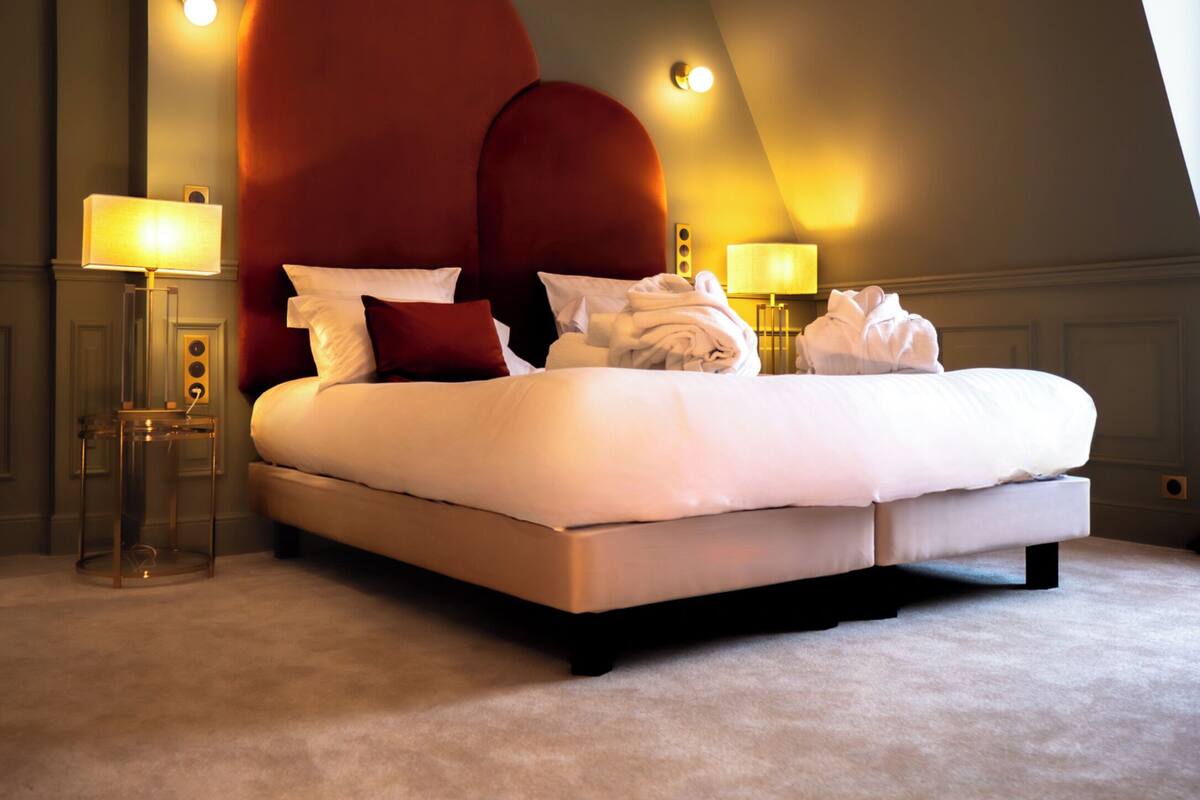 Una cama grande con cabecera roja, dos lámparas de noche y piso cubierto de alfombra.