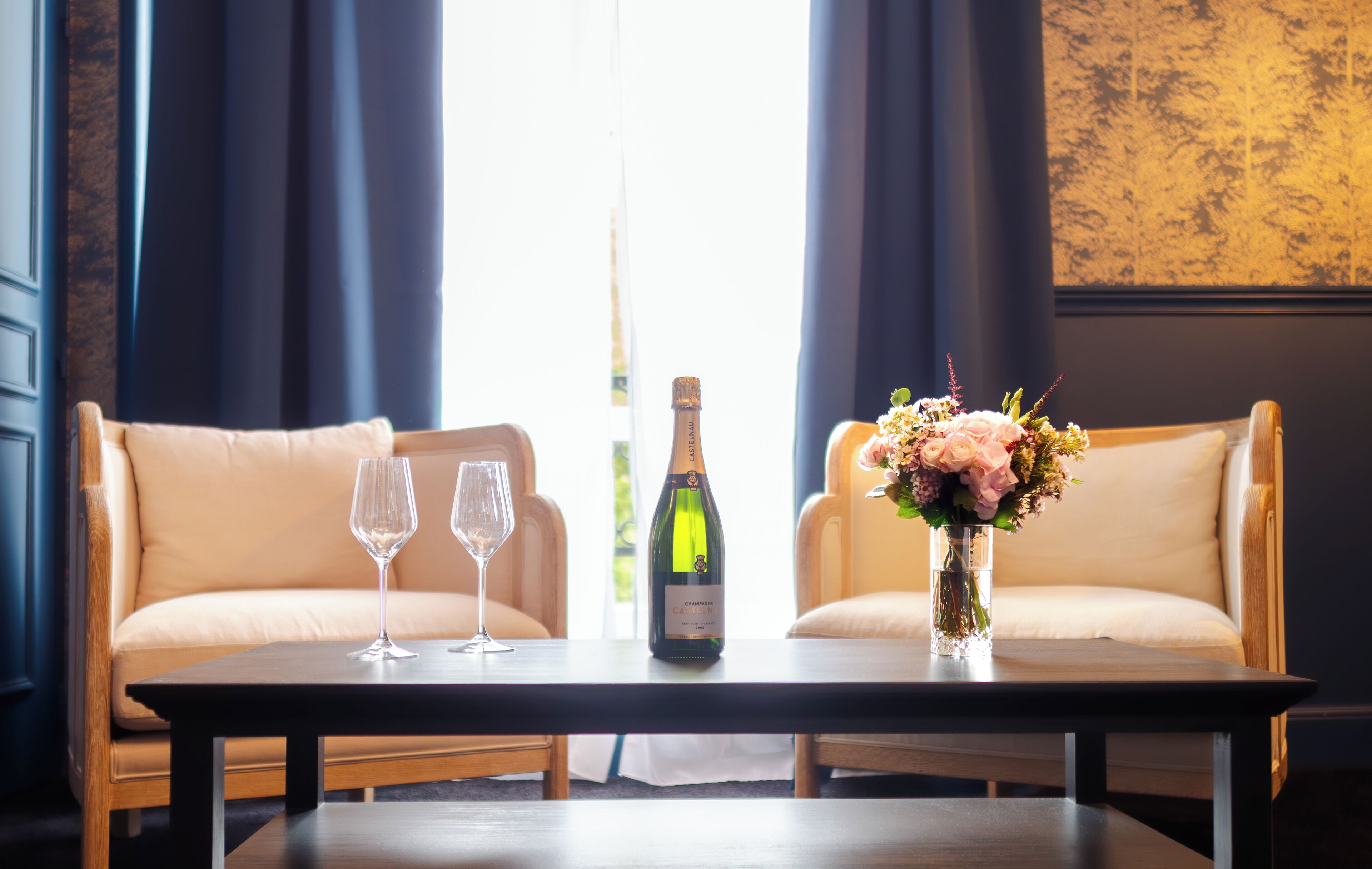 A room with two sofas, a table, two wine glasses, a bottle of champagne, and a vase with flowers.