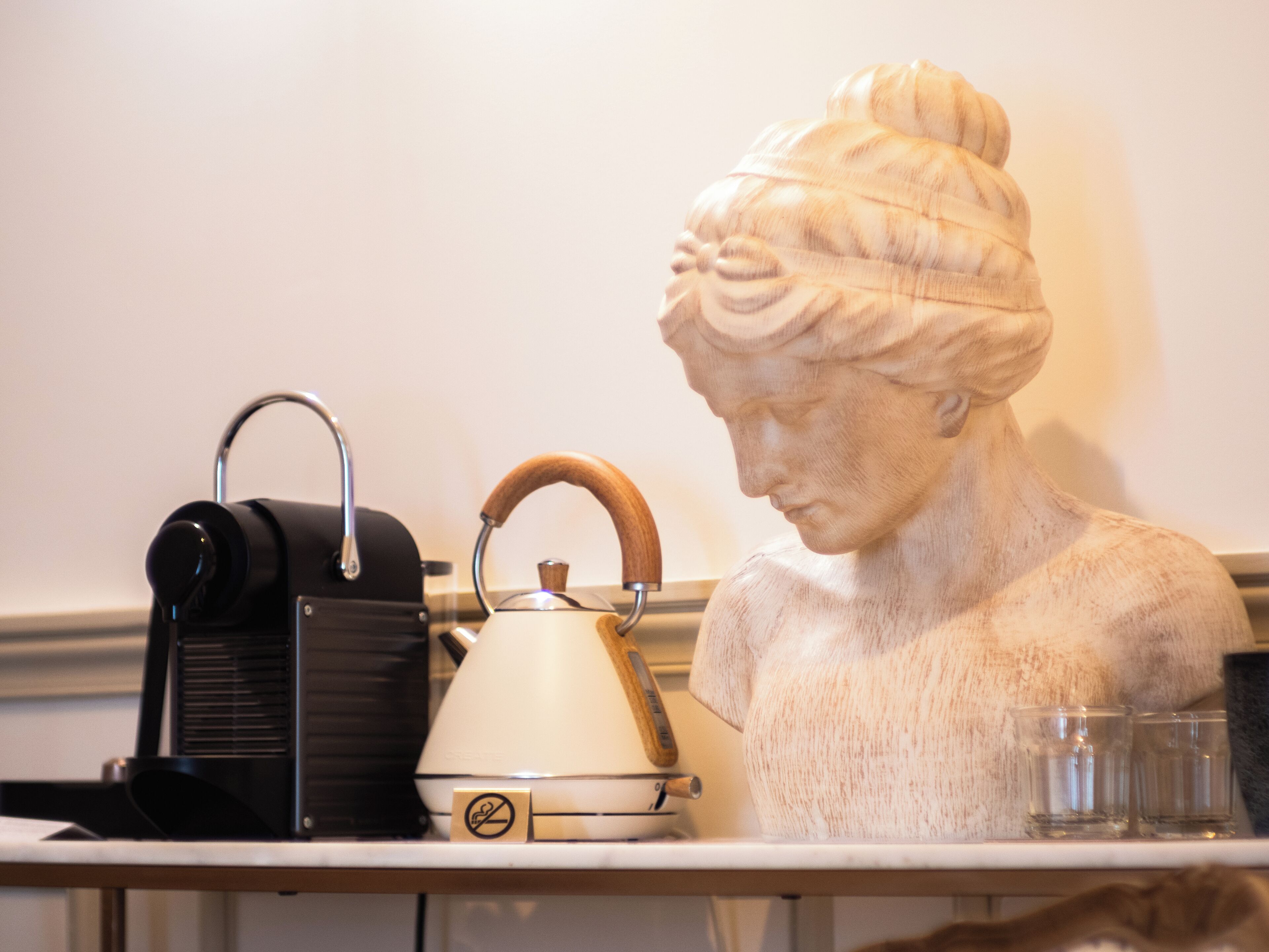 Un busto, una tetera eléctrica antigua y dos vasos sobre una mesa.