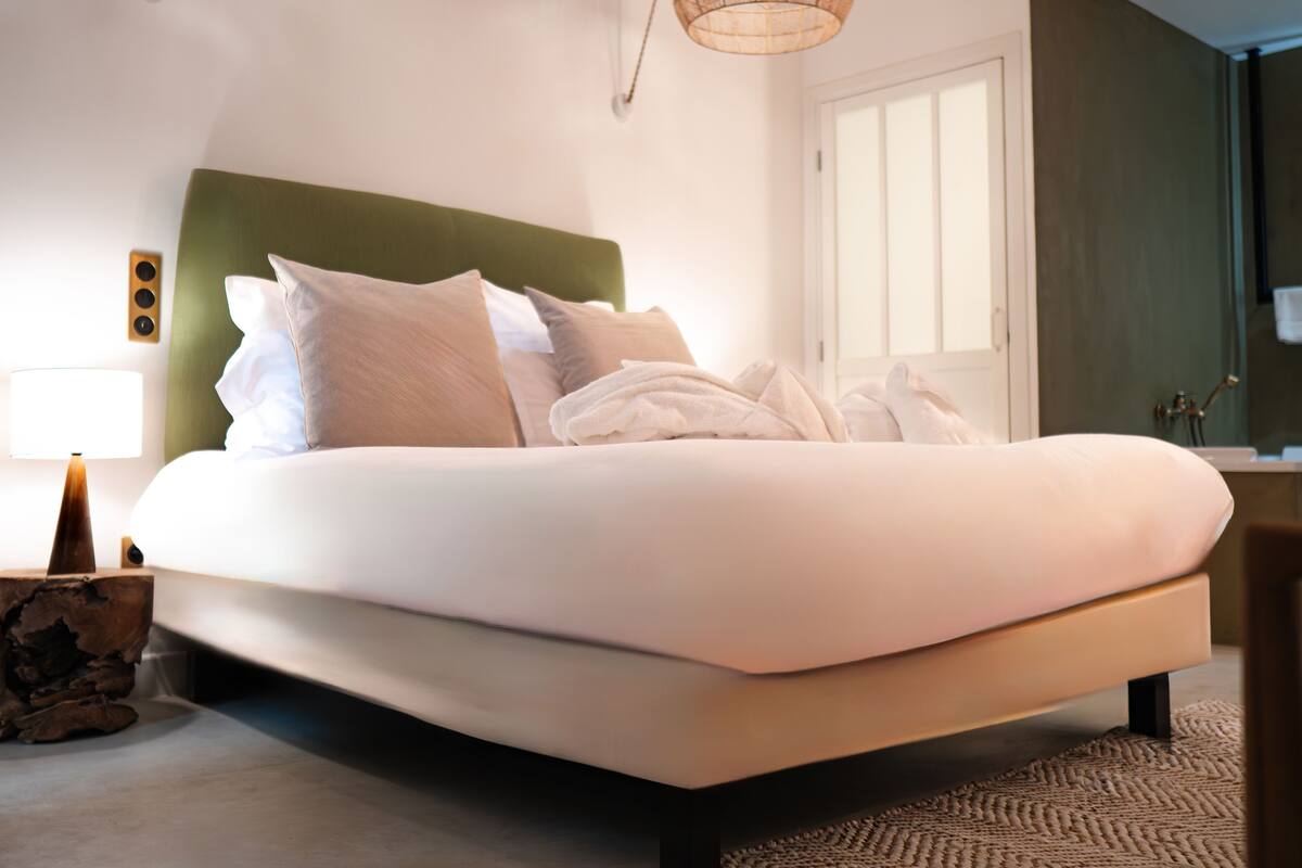 Un dormitorio moderno con una cama grande, cabecera verde, lámpara de noche y un ventanal amplio.