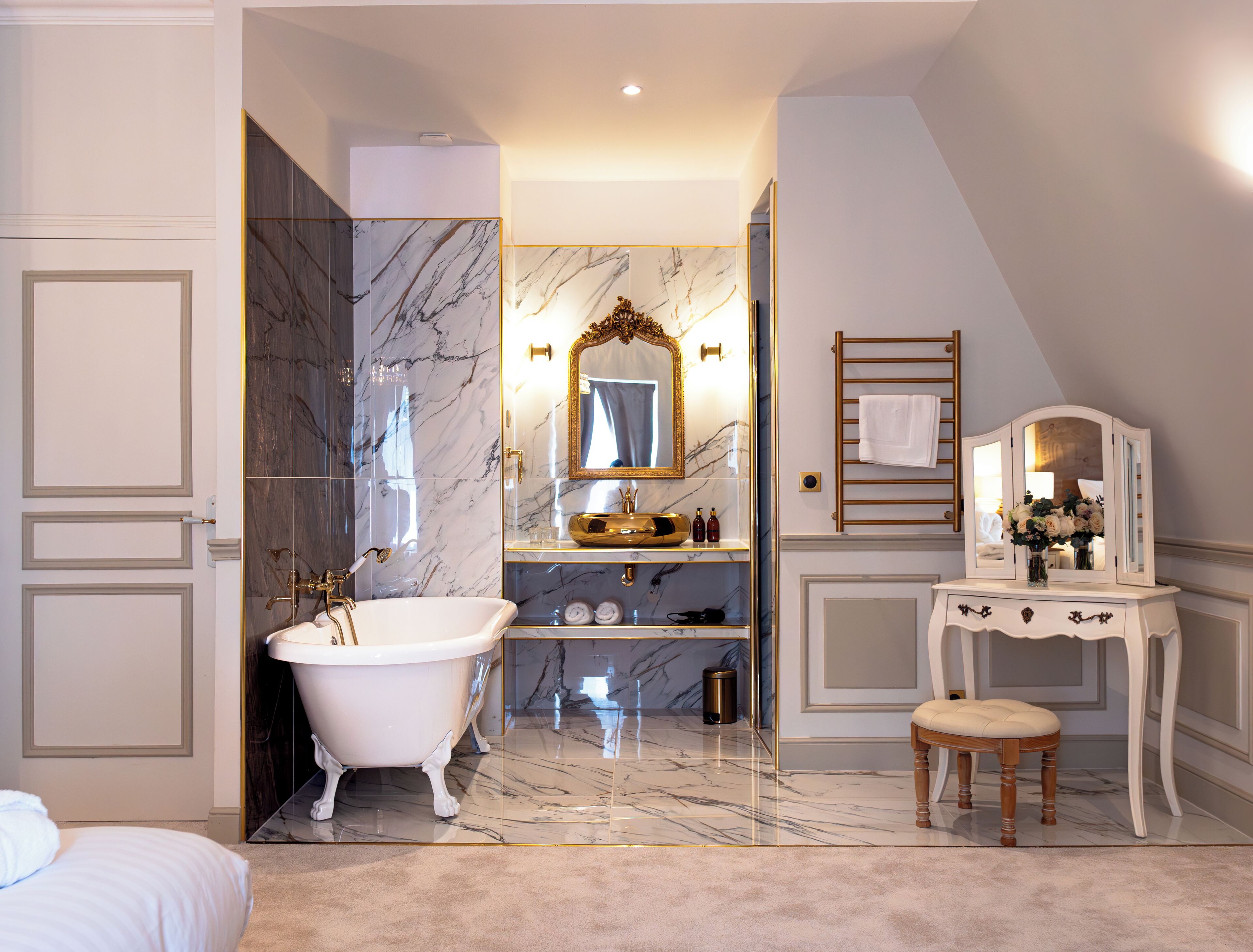 A luxurious bathroom with a freestanding bathtub, marble walls, a vanity with a mirror, and a towel rack.