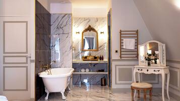 A luxurious bathroom with a freestanding bathtub, marble walls, a vanity with a mirror, and a towel rack.