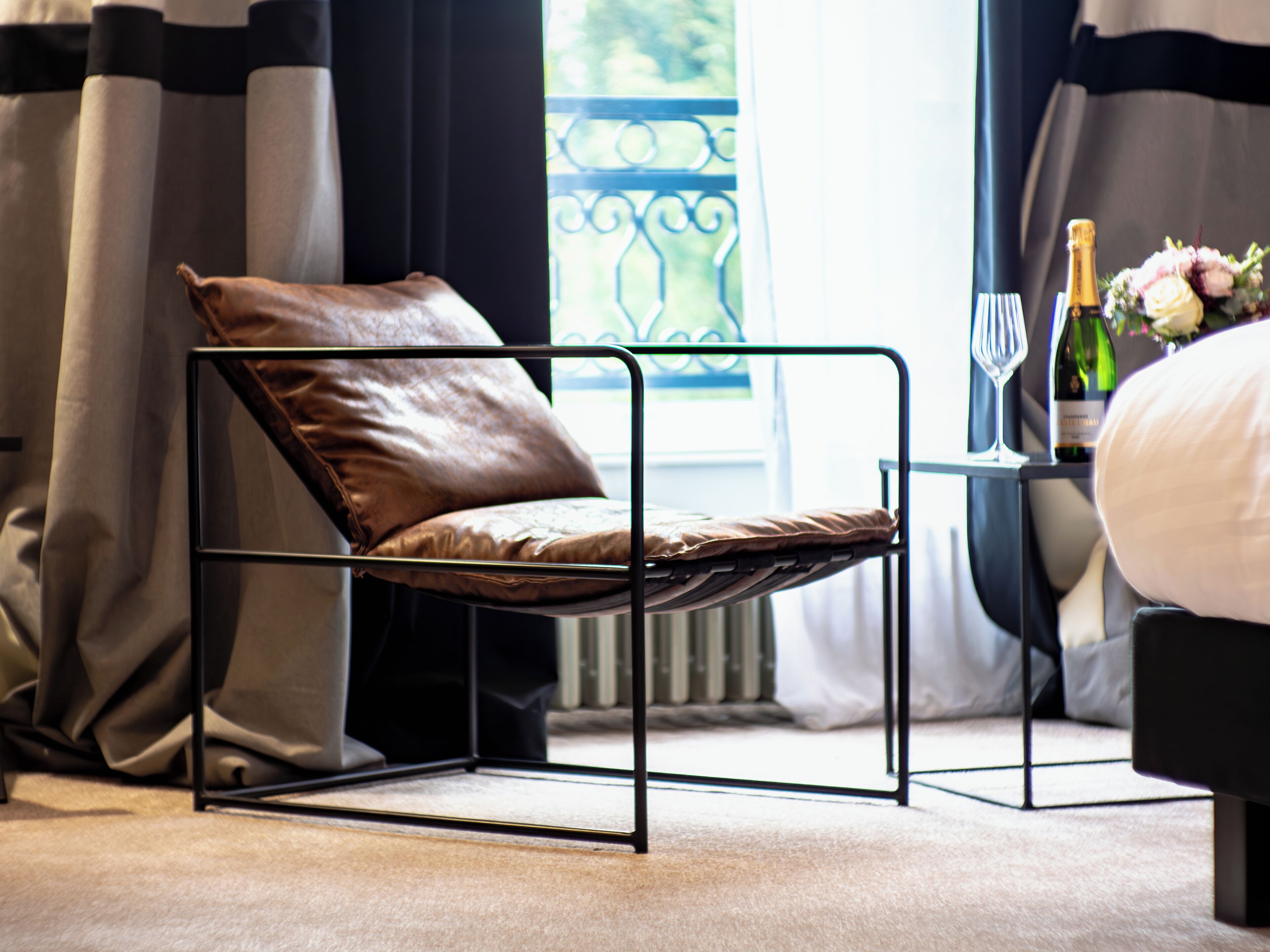 A modern room with a leather chair, a small table with a bottle and glass, and a bed with white bedding.