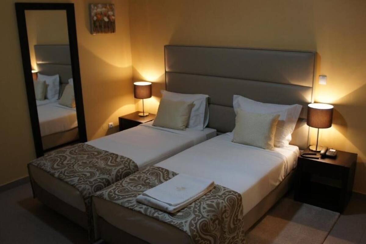 A double bed with a patterned bedspread, two bedside tables with lamps, a large mirror on the wall, and a small rug on the floor.