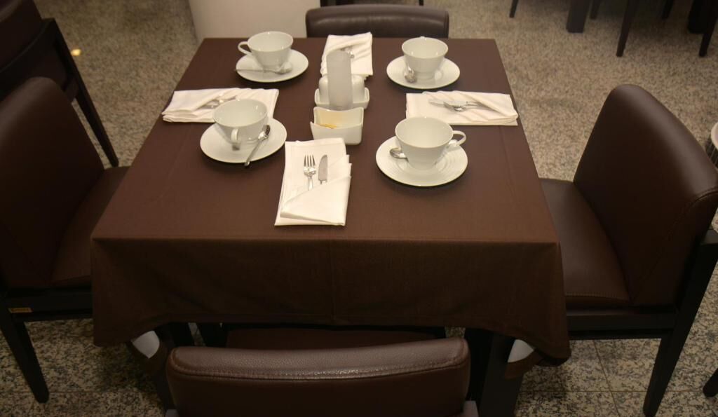 Taula de menjador coberta amb tasses, platets i coberts blancs, envoltada de cadires de cuir marró.