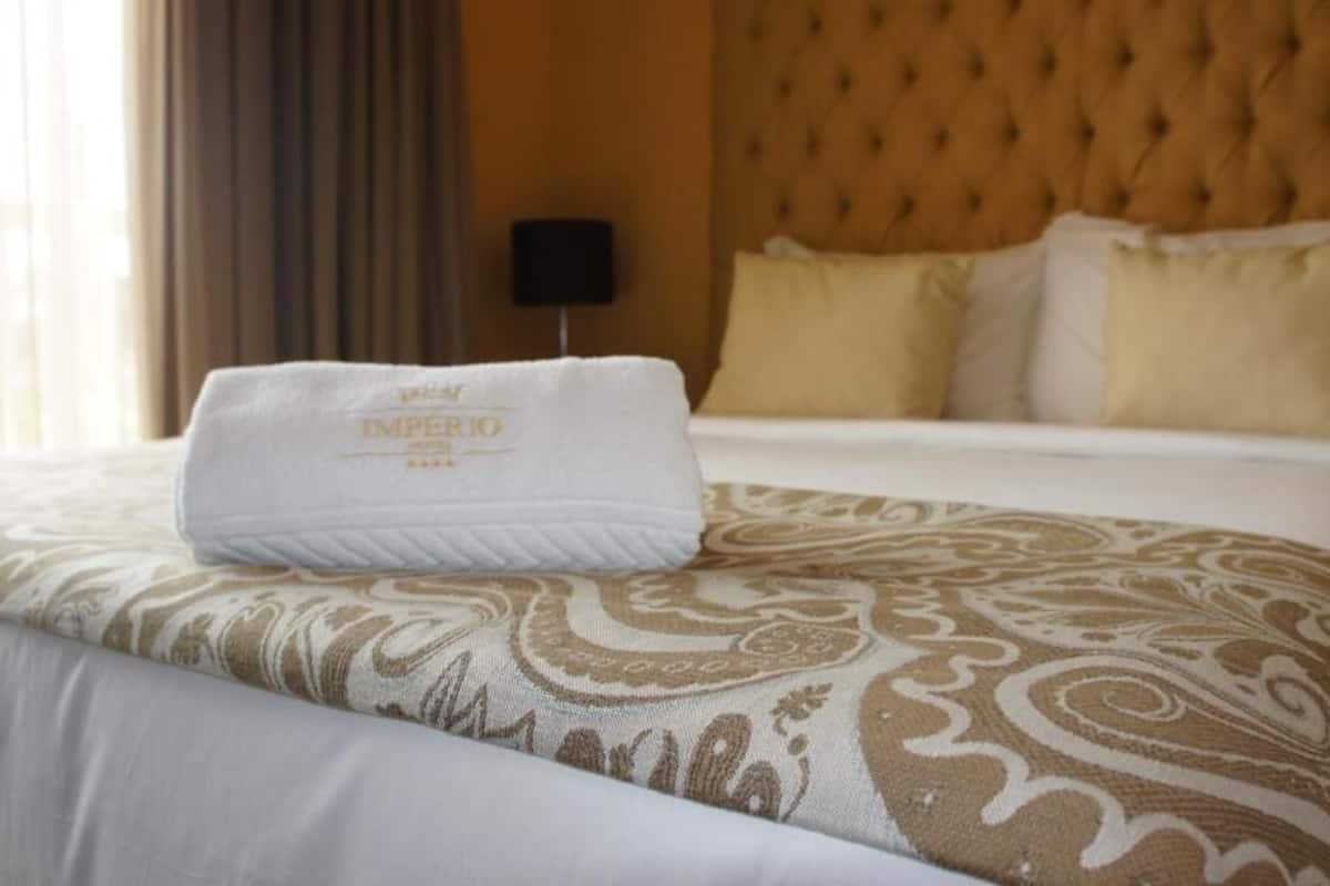 A hotel room with a neatly made bed, a tufted headboard, and a decorative throw pillow.