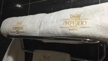 A white towel with "IMPERIO HOTEL" and a crown logo hanging on a metal towel rack.