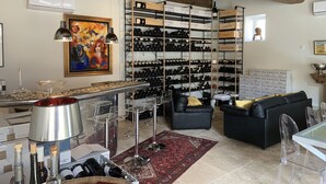 A wine cellar with shelves of bottles, a dining area with clear chairs, and a painting on the wall.