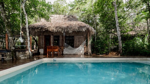 A pool area with a thatched-roof hut, wooden deck, and surrounding trees. - Aldea Colibrí (Tulum)