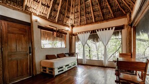 A room with a wooden bed, a dining table, and a thatched roof. - Aldea Colibrí (Tulum)