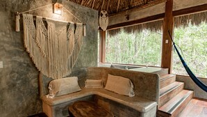 A room with a stone bench, a wooden stool, macramé wall hangings, and a hammock. - Aldea Colibrí (Tulum)