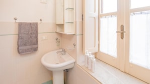A bathroom with a sink, mirror, towel rack, and a window with curtains. - Casa Gallizza con Vista Mare by Wonderful Italy (Cefalù)