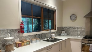 A modern kitchen with a window, stainless steel appliances, and decorative items on the counter. - Brook Cottage@FernglenForestRetreat (Mount Dandenong)