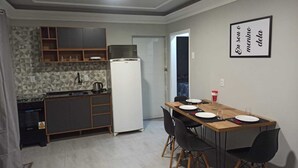 A compact kitchen with a refrigerator, stove, and microwave. There is a dining table with chairs and a framed sign on the wall. - Leandro's Residence. Casa em Balneário Camboriú Para Aproveitar com a Família! (Balneário Camboriú)