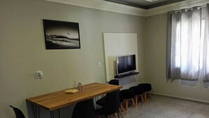 A dining area with a wooden table and black chairs, a flat-screen TV mounted on the wall, and a window with curtains. - Leandro's Residence. Casa em Balneário Camboriú Para Aproveitar com a Família! (Balneário Camboriú)
