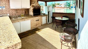 Een keuken met een tegelachtergrond, een ingebouwde oven en een koelkast. Er is een eethoek met rieten stoelen en een tafel.