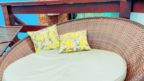 Een rieten lounge stoel met een kussen en twee sierkussens met bloemen.