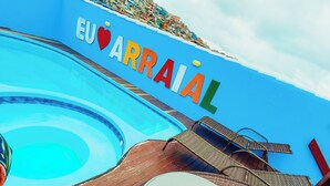 Een zwembadgedeelte met een blauwe muur en de woorden 'EUARRAÍAL' in kleurrijke letters. Er staan rieten lounge stoelen en kussens.