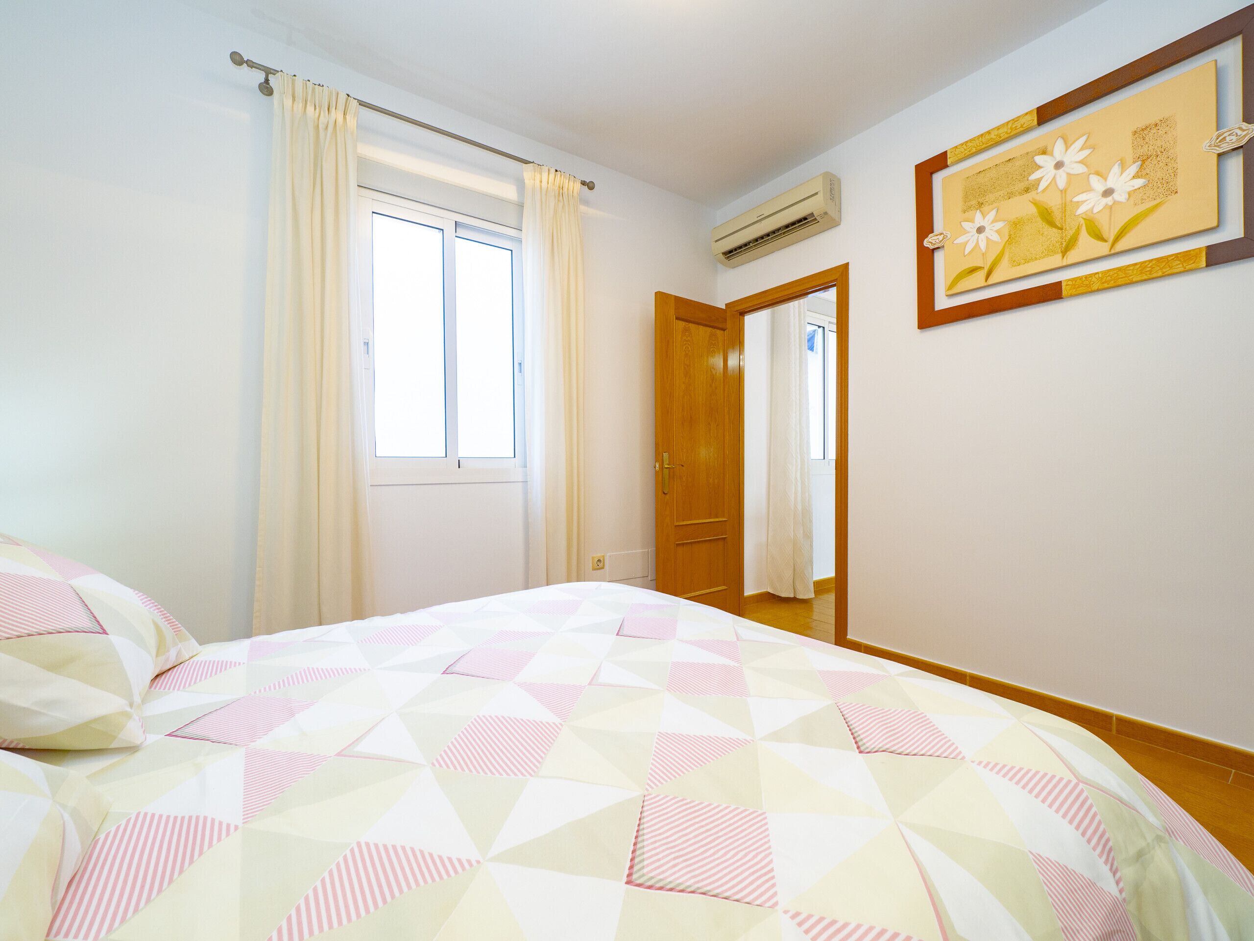 Une chambre à coucher avec un lit, une fenêtre avec des rideaux, un appareil de climatisation et une porte.