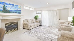 A living room with a fireplace, a sofa, a patterned rug, and a large painting on the wall. - ❤️Spacious Home in Heart of Vancouver--Easy Access to Everything❤️ (Vancouver)