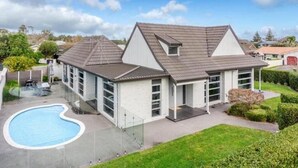 Een modern huis met twee verdiepingen, een zwembad, grote ramen en een verzorgd gazon.