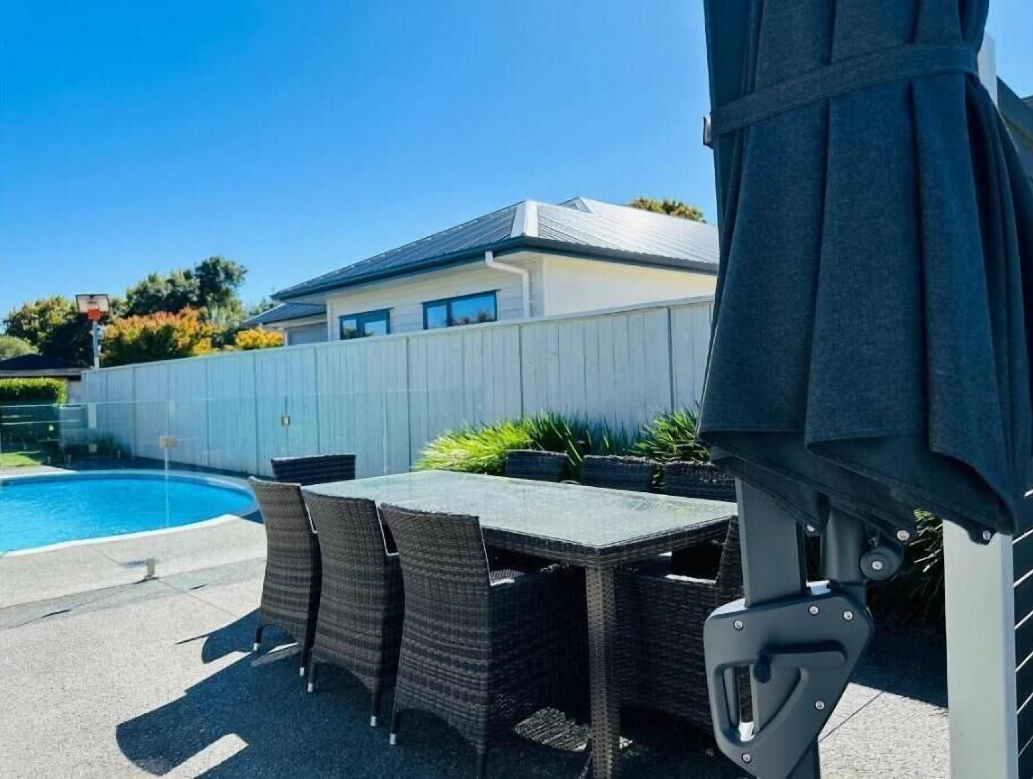 Un jardin avec une piscine, une table et des chaises sur une terrasse couverte.