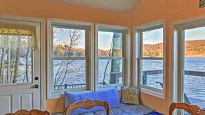 A cozy room with a large window overlooking a lake, a wooden bench with cushions, and a door with a curtain. - Waterfront Cottage 10 Min From Great Barrington (New Marlborough)