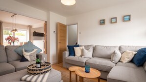 Una sala moderna con un sofá gris, una mesa de centro y una mesita auxiliar. Hay tres cuadros enmarcados en la pared.