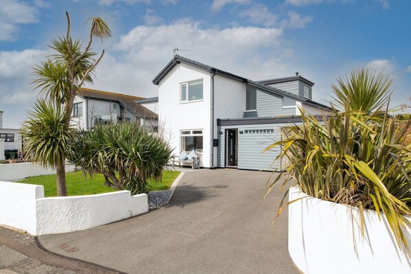 A two-story residential house with a garage, a driveway, and a well-maintained lawn with palm trees.