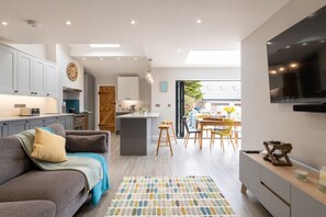 A modern kitchen with a central island, a dining area with chairs, a sofa with a throw blanket, and a flat-screen TV mounted on the wall. - Fronallt: A fabulous 3 bedroom property in Rhosneigr (Rhosneigr)