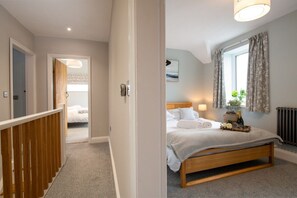 A bedroom with a wooden bed, a window with curtains, a radiator, and a nightstand with a bottle and flowers.