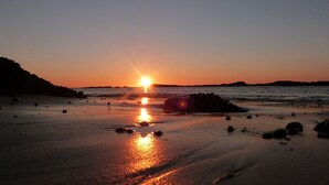 Une plage au coucher du soleil, où le soleil se reflète sur le sable et les rochers humides.