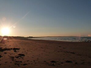 A beach with footprints leading to the water, a clear sky, and the sun setting or rising.