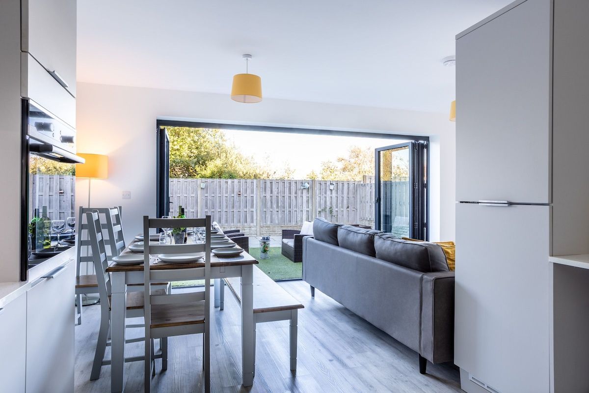 A modern kitchen with a dining area, a grey sofa, and a view of the backyard.