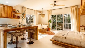 A modern, well-lit room with a dining area, a sofa, and a large bed. - Kite Beach Suite with Work Space and Full Kitchen (Cabarete)