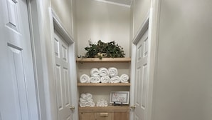 A narrow hallway with white doors, a wooden cabinet with towels, and a welcome sign. - All You Ever Wanted "The White House" (Columbia County)