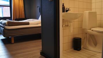 A hotel room with a bed, a window with curtains, a sink, and a toilet.