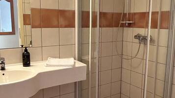 A bathroom with a glass-enclosed shower, a white sink with a mirror, and a toilet.