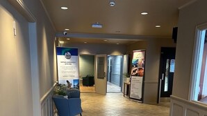 A hotel corridor with a reception desk, a blue chair, and a sign about a nature experience. - Marina Hotel Sortland (Sortland)