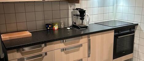 A modern kitchen with light wood cabinets, a black countertop, and a tiled backsplash.