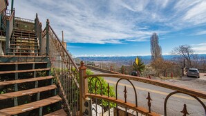 Una escalera con barandilla metálica que conduce a un camino con vistas a montañas distantes.