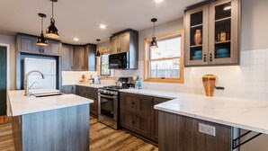 Una cocina moderna con armarios de madera oscura, encimera blanca, electrodomésticos de acero inoxidable e iluminación colgante.