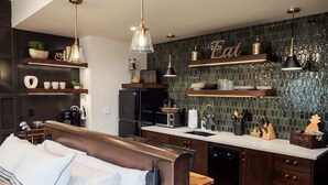 Eine moderne Küche mit dunklen Holzschränken, einer weißen Arbeitsplatte und einem eingebauten Backofen. Es gibt einen Essbereich mit einer hölzernen Bank und weißen Kissen.
