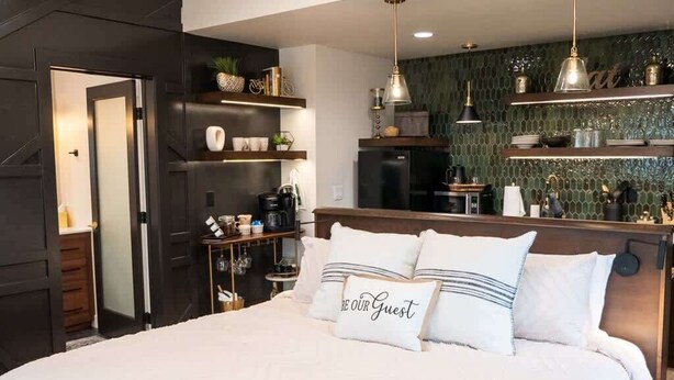 Ein modernes Schlafzimmer mit einem großen Bett, einem Einbauschrank, einer Küchenzeile und einer auffälligen, grünen Mosaikrückwand.