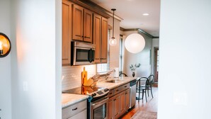 Une cuisine moderne avec des meubles en bois, des appareils en acier inoxydable et un grand luminaire suspendu.