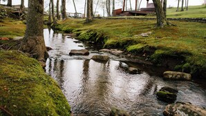 Ein friedlicher WaldBach mit moosbewachsenen Steinen und einem hölzernen Pavillon im Hintergrund.