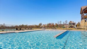 Ein rechteckiger Swimmingpool mit klarem, blauem Wasser, umgeben von einem Zaun, und ein kleines Gebäude mit Dach im Hintergrund.