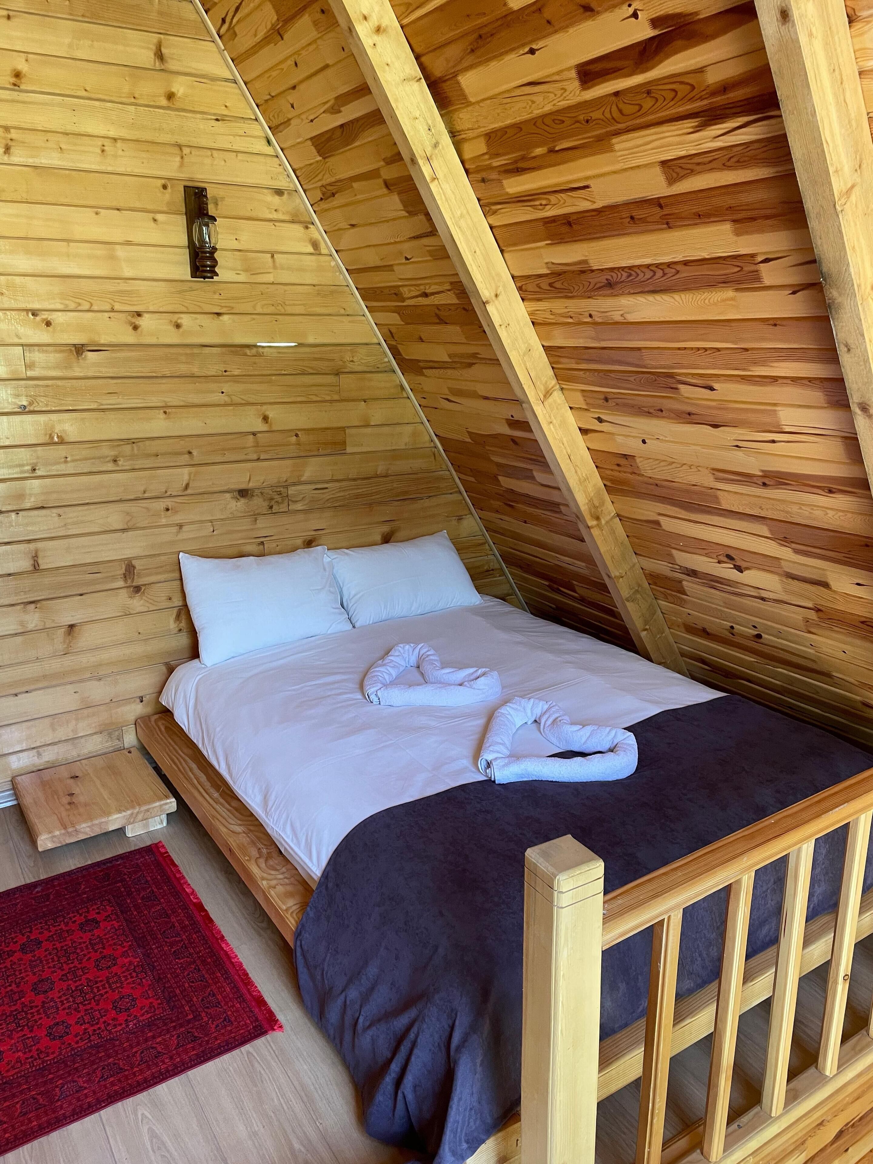 A wooden room with a bed, a nightstand, and a red rug.