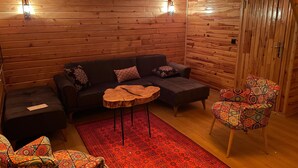 A cozy log cabin interior with a dark sofa, a patterned armchair, a wooden coffee table, and a red rug. - Bizim O'ra Küme Evleri & Bungalov (Maçka)
